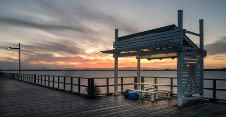 Naklejka premium Woody point jetty at sunset with fishing tackle ready for fishing