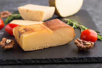 Smoked cheese and various types of cheese with rosemary and tomatoes on black slate board on a black concrete background. Side view, selective focus.