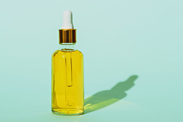 cosmetic bottle with pipette and yellow oil on blue background with shadow