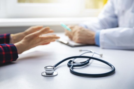 Medical Consultation - Doctor Talking To Patient In Clinic Office. Focus On Stethoscope