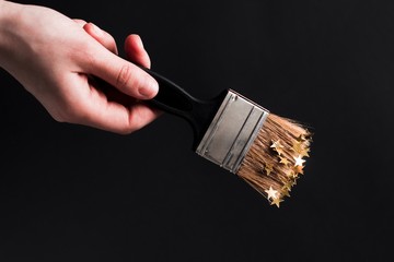 young woman holding a black brush covered with gold paint with gold stars on black background