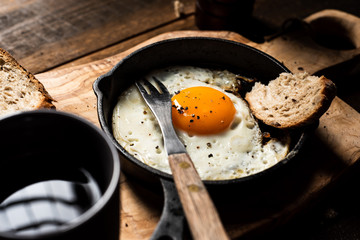 Fried egg, bread slice and black coffee.Chopping board. Dark, wooden, rustick table.