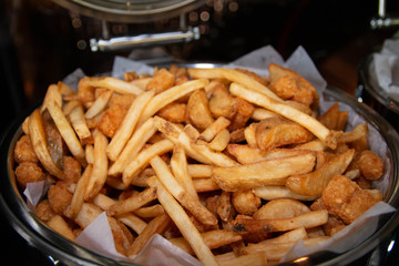 French fries and deep fried potato wedges mixed in a large buffet tray.