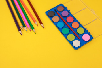 A palette of paints for drawing and color pencils on a yellow background, space for text. Flat lay.