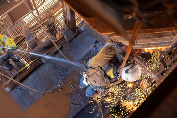 Work safety practise spotter, firewatch personal holding firehose spraying water  at the conveyor belt to stopping controlling fire during welder wearing PPE conducting oxy cutting metal repairing    