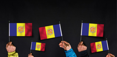Fototapeta na wymiar Hands holds flags of Andorra on dark background