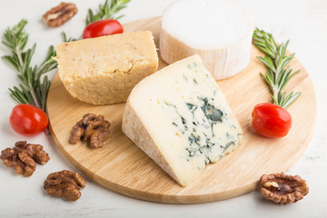Blue cheese and various types of cheese with rosemary and tomatoes on wooden board on a white background . Side view, selective focus.