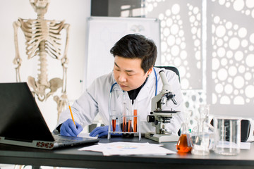 Young Asian Korean male virology scientist makes notes, working on development of new vaccine or medicine to prevent and treat new type of corona virus. Medicine, healthcare, virology concept