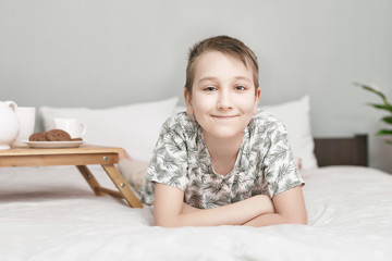 Portrait of boy lying in bedroom alone, looking on camera. The boy woke up joyful. Child morning on bed at home. Good happy morning in the nursery. Portrait of smiling boy.