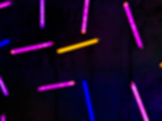 Blurred colourful neon light sticks in pink, yellow and blue on dark surface for texture and background.