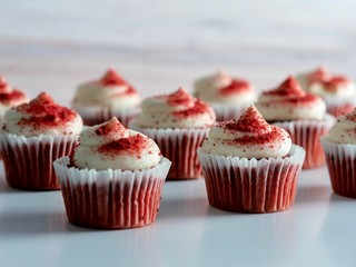 Red velvet cupcakes lined up with white frosting and red powder sprinkles, delicious and yummy on a white and wooden background.