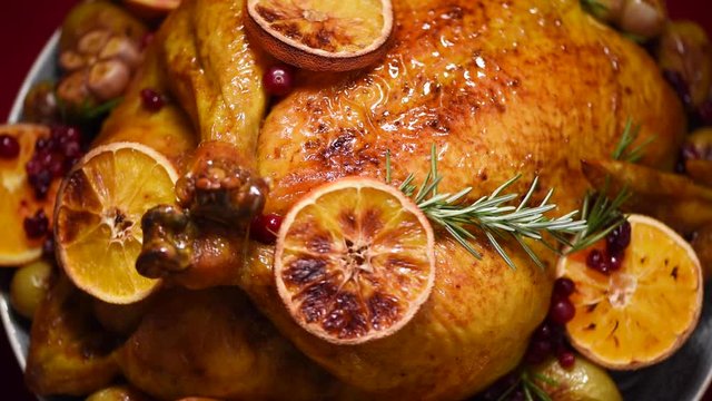 Christmas family dinner. Roasted chicken with herbs, oranges, cranberries on rotating background, slow-motion shooting.