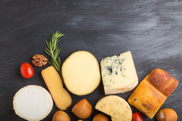 Set of different types of cheese with rosemary and tomatoes on a black wooden background . Top view, copy space.