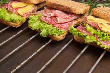 Grilled sandwiches with  salami, cheese and salad on metal grill