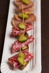 Assortment of canapes with bacon, cheese, pickles on white plate
