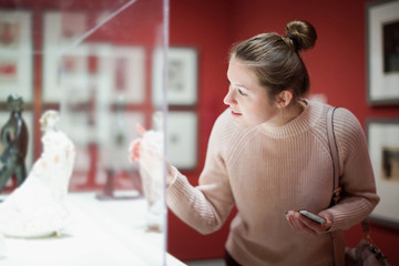 Young woman visitor using  phone  in museum - obrazy, fototapety, plakaty