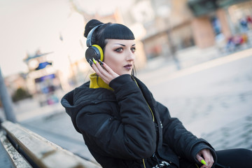 Beautiful gothic girl listening her music by headphones and walking around the city