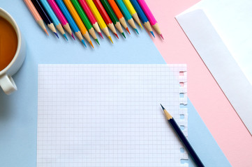 Top view of a sheet of paper, colored pencils, an envelope and a Cup of tea on the table. Write a letter. 