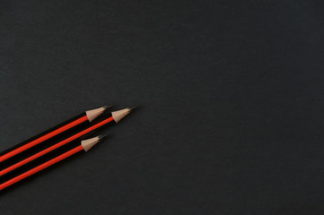 Three lead pencil with black and red stripes on a dark background to spiral upwards like a rocket