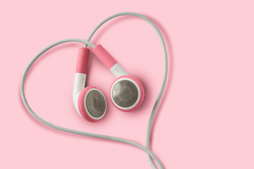 Pink earphones in heart shape on pink background - Concept of love, listening and support to women