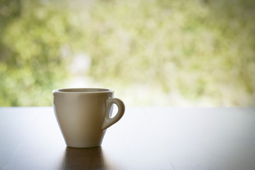 White coffee cup on wooden table with beautiful nature bokeh background.