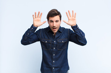 young handsome man screaming in panic or anger, shocked, terrified or furious, with hands next to...