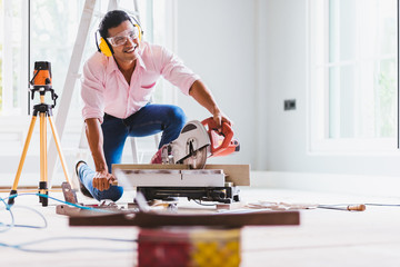 Smart indian contractor hand using sawing machine wood work and working overall equals a wooden bar in the house renovation background. Home improvement ideas concept.