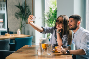happy romantic couple taking picture with mobile phone in cafeteria