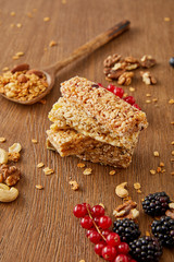 Selective focus of cereal bars, spatula with granola and redcurrants, blackberries, cashews, walnuts on wooden background