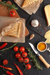 Appetizing sandwiches with tomato cheese and herbs with ingredients on a black wooden table