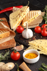 Appetizing sandwiches with tomato cheese and herbs with ingredients on a black wooden table