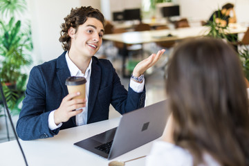 Beautiful young business woman and handsome businessman in formal suits are using a laptop, talking and smiling while working in office