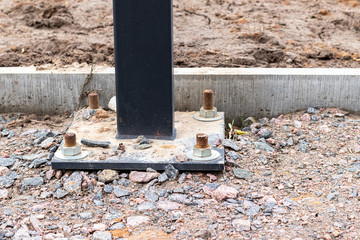 Installation of a lighting column or billboard with four anchor bolts on a track of a construction site covered with gravel near a concrete curb
