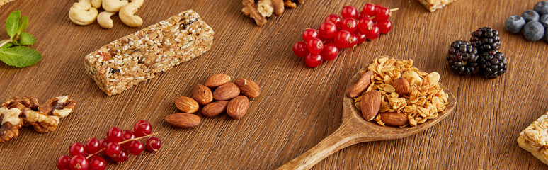 Berries, nuts, cereal bars and spatula with granola on wooden background, panoramic shot