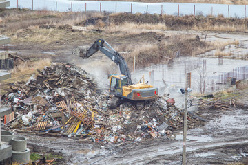 Yellow excavator picks up construction waste for loading onto a truck. Technique destroyed the building, is reinforcement, concrete and stones. Destroyed house, concrete, fittings, dust flies.