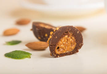 Chocolate caramel ball candies with almonds on a white wooden background. Side view, selective focus.