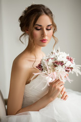 Close up portrait of young bride in a beautiful dress holding a bouquet of flowers in bright white studio. Wedding concept.