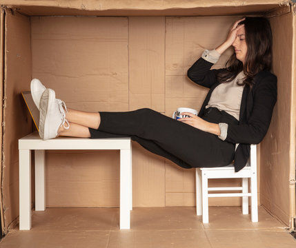 stressed out businesswoman sitting in cramped craton office, holding a coffee cup