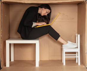 young beautiful businesswoman sitting in office cardboard box, working on laptop