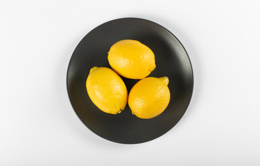 Lemons in a black saucer isolated on white background. top view