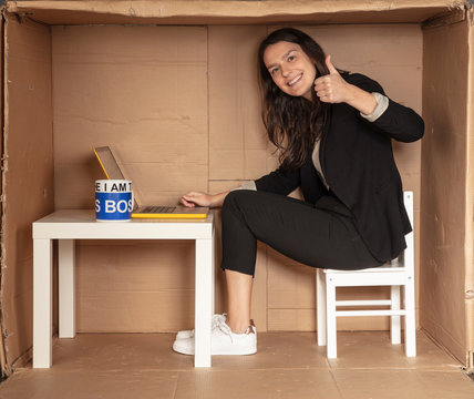young beautiful businesswoman sits in office cardboard box and shows thumb up