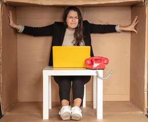 beautiful businesswoman sits in a tight paper office, needs more space, pushes the walls