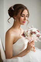 Obraz na płótnie Canvas Close up portrait of young bride in a beautiful dress holding a bouquet of flowers in bright white studio. Wedding concept.