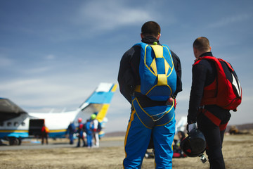 Figures of two skydivers with parachutes preparing for take-off against a background of an airplane...