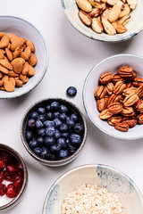 Ingredients for homemade granola: oatmeal, dried cherry, pecans, almond, brazilan nuts, blueberries in a bowls on grey background. Healthy diet breakfast. Flatlay. Top view. Selective focus