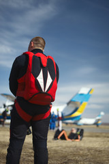 Naklejka premium Figure skydiver with a parachute preparing for take-off against a background of an airplane and a blue sky, back view. Parachute jumping.