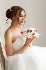 Close up portrait of young bride in a beautiful dress holding a bouquet of flowers in bright white studio. Wedding concept.