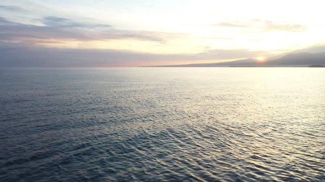 Aerial drone view of sunset over sea, the drone flies close to the ocean in asia towards sunset and beautiful mountains and volcano.