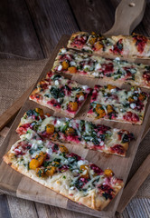 Top down view of slices of vegetable flatbread pizza on a wooden cutting board.