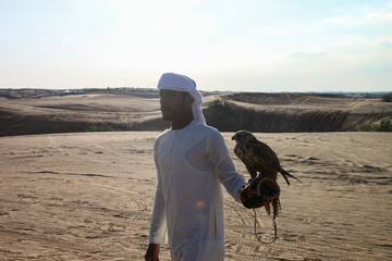 Arab man dressed in white walking through the desert with an eagle on his arm